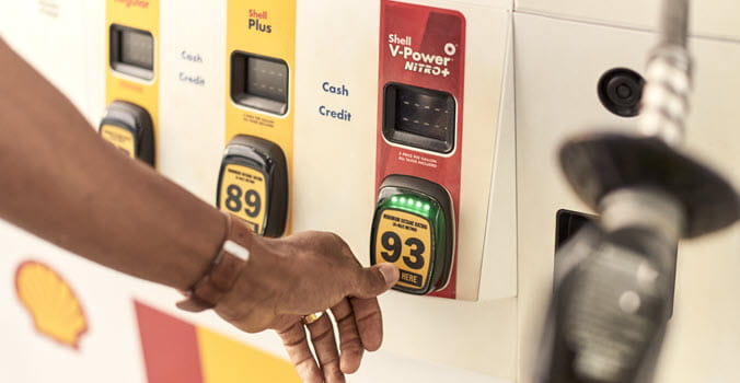 close up of a gas pump with a person's arm reached out to select their fuel grade