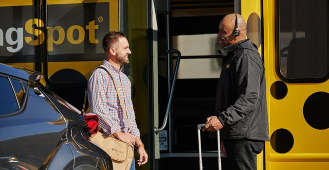 Two men standing outside of The Parking Spot yellow and black spotted shuttle appearing to be having a nice conversation before boarding shuttle to airport with luggage