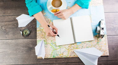 Overhead look of man with travel plans, cup of coffee, notepad, camera and map on a desk