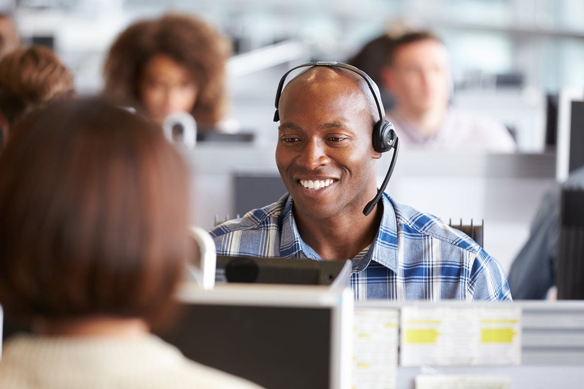 A smiling customer service representative wearing a headset and a plaid shirt.