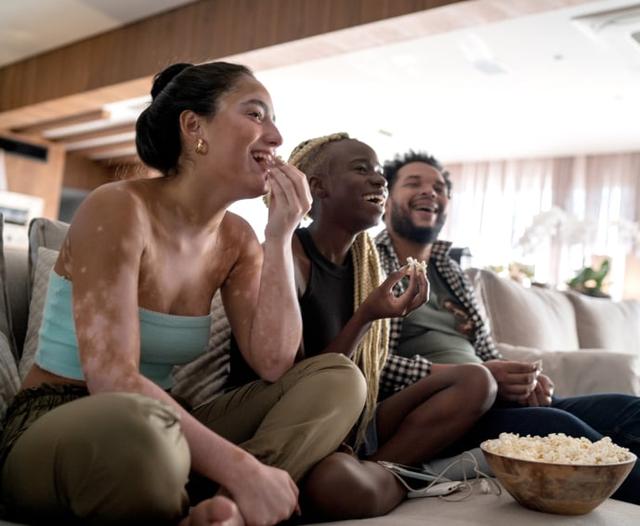 Friends eating popcorn on couch while watching a movie