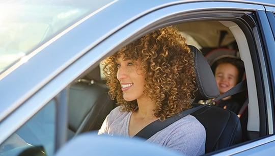 A woman driving in a car with a little boy in the backseat in a car seat.