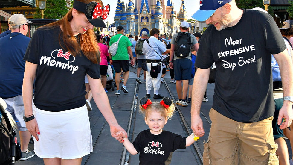 Mom and dad holding little girl's hand, all three wearing matching Disney t shirts
