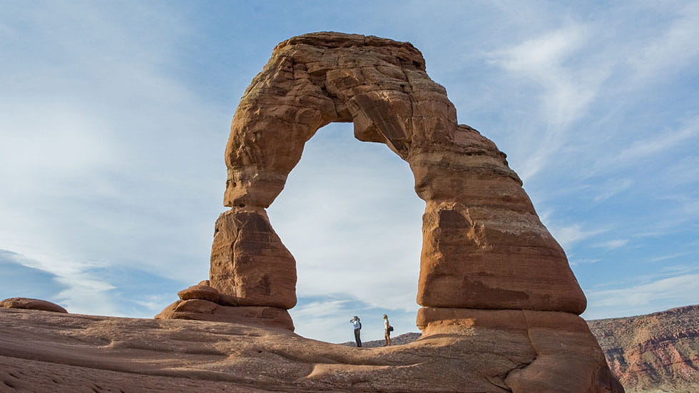 Hikers stand under Delicate Arch - Arches Natioanl Park