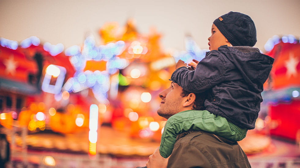 Father with son on shoulders looking up at lights