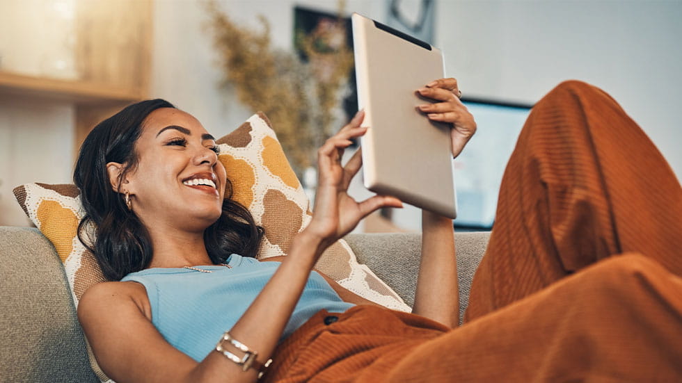 woman smiling on couch holding tablet 