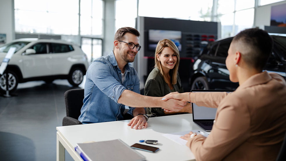couple at car dealership shaking hands with salesman 