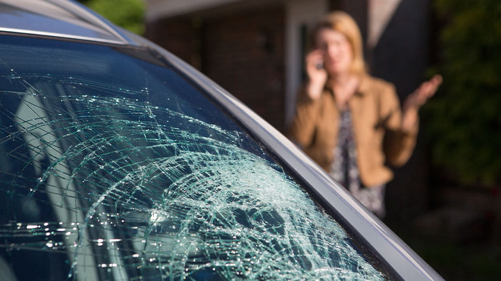 broken car windshield with woman on phone in background