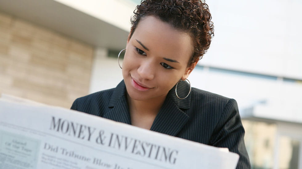 woman reading money and investment section of newspaper