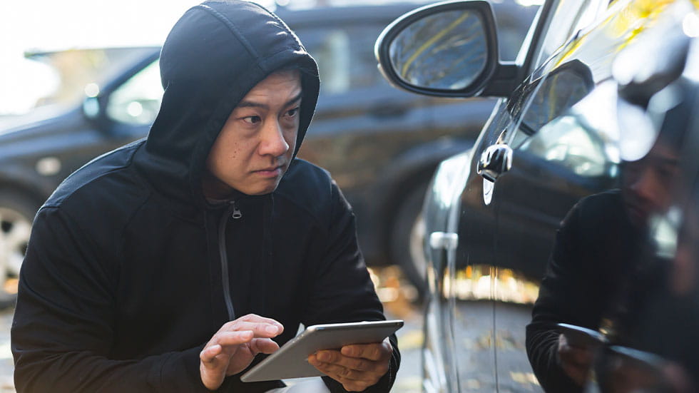 Hacker with tablet near a parked car