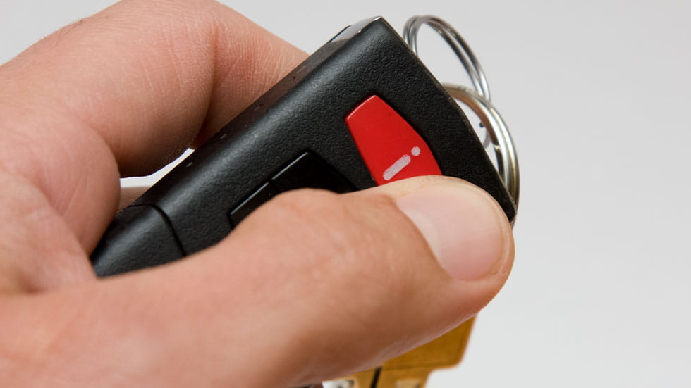 finger holding onto panic button on car fob