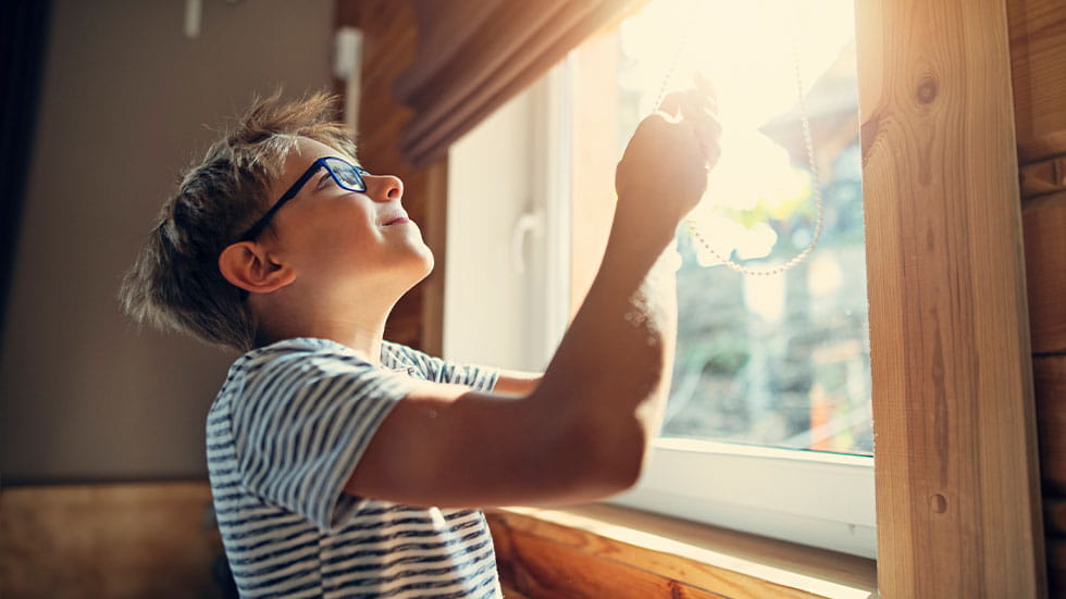 kid opening blinds to let light in