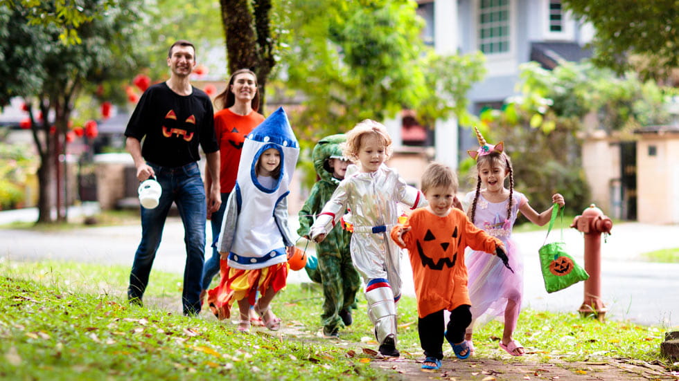 Parents and children walking down sidewalk, dressed in Halloween costumes