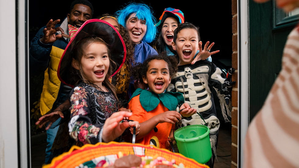 Children dressed in Halloween costumes in doorway getting candy