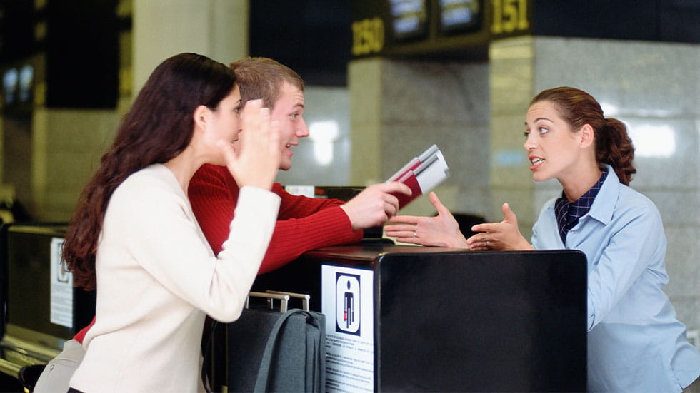 Frustrated man and woman in airport holding credit card while speaking to worker