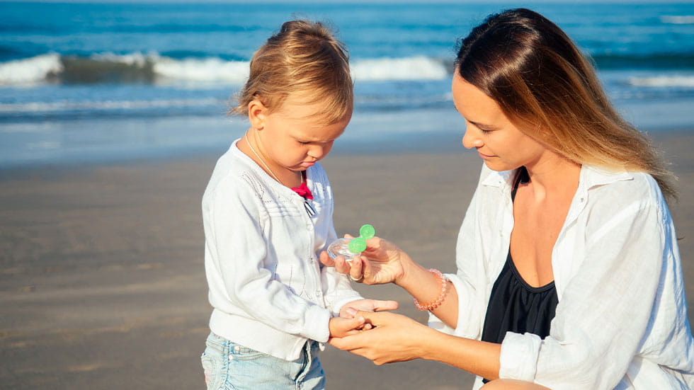 mom applying hand sanitizer on kid's hands at beach
