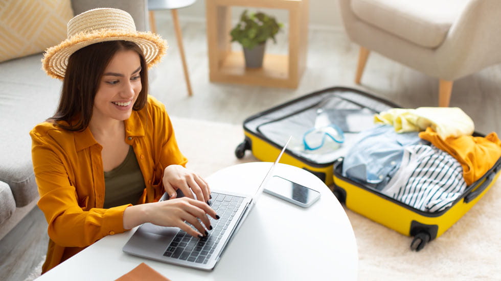 Woman on laptop with open suitcase next to her