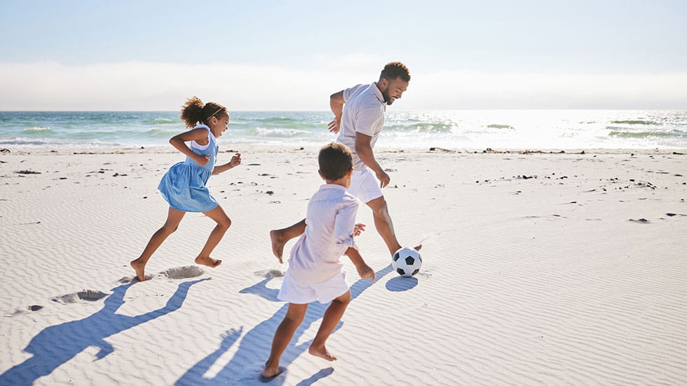 Father and two children playing soccer on the beach