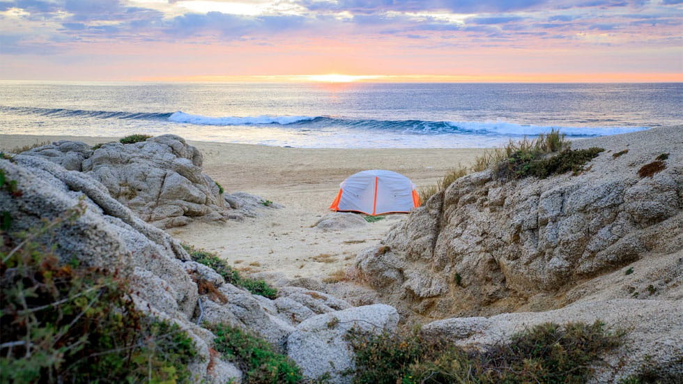 Tent pitched near the ocean with a sunrise in the background