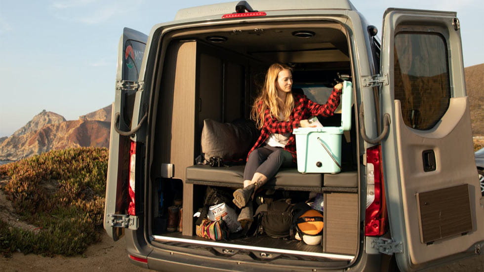 Woman looking through cooler while sitting in van