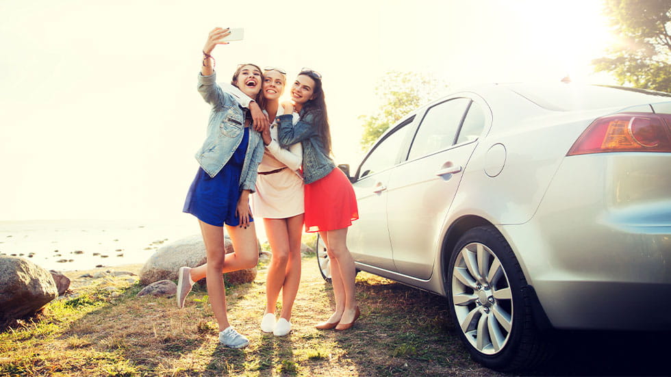 3 girls taking selfie next to car