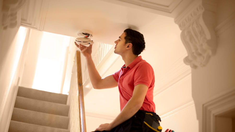 Man checking a smoke detector in a hallway of a home