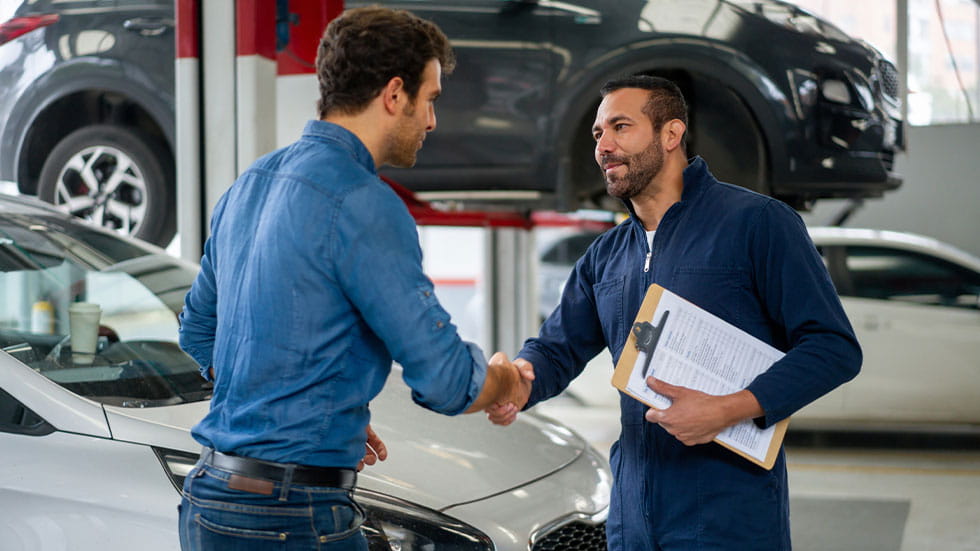 man in auto repair shop shaking hands with mechanic