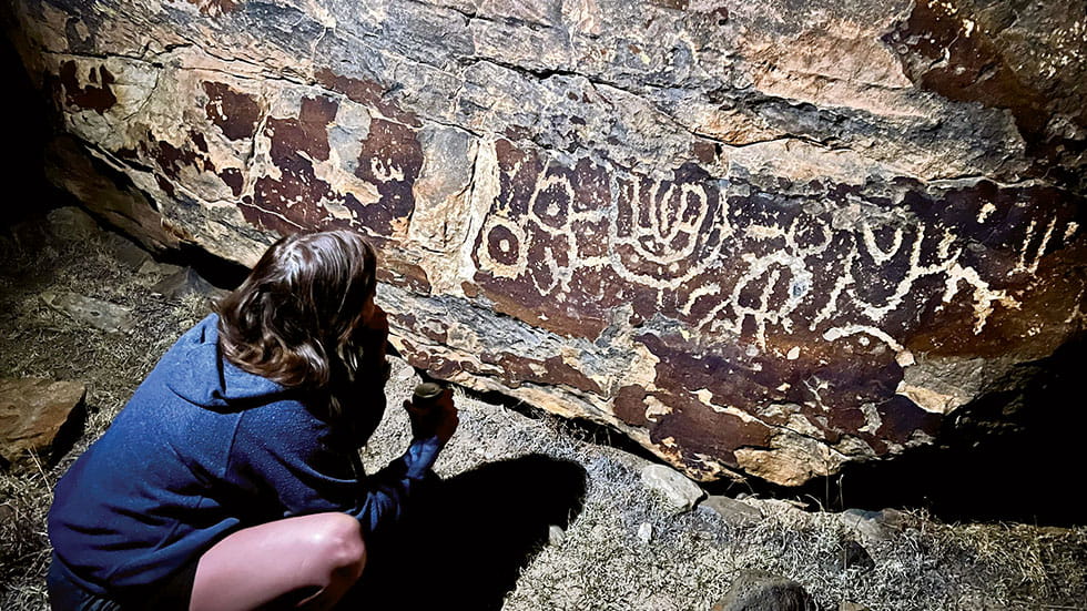 A visitor studies petroglyphs carved into a rock at Black Mesa State Park and Preserve. Photo by Emily Brashier