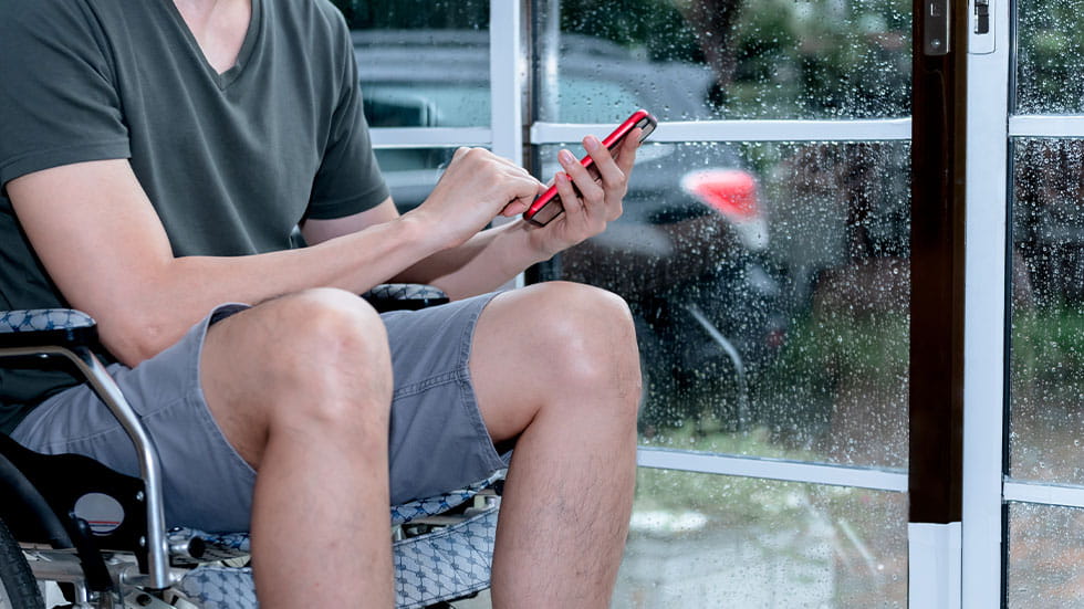man on wheelchair checking phone while it is raining outside