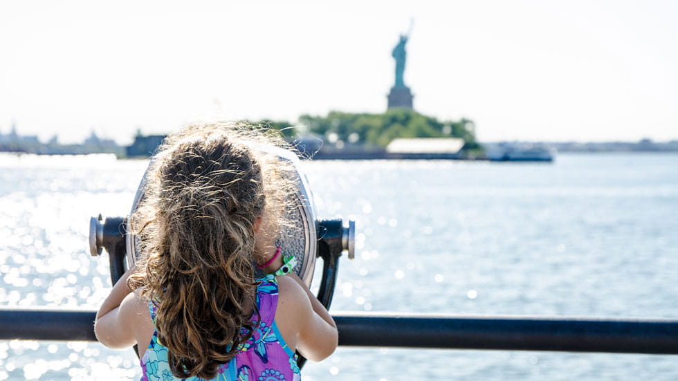 Girl looking through view finder at the Statue of Liberty in NYC