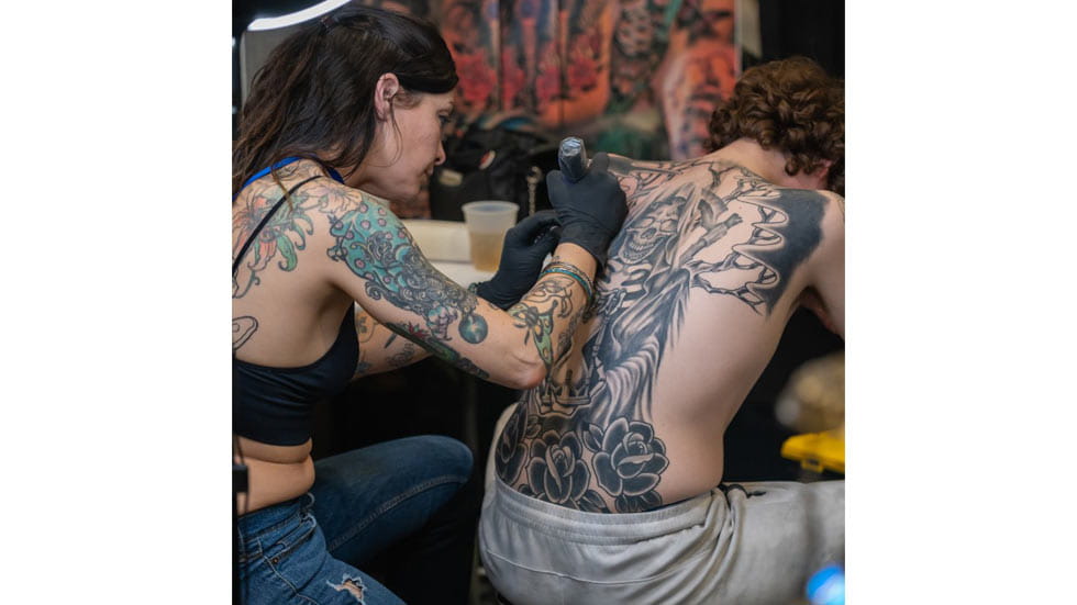 Woman giving man a back tattoo at a tatoo convention