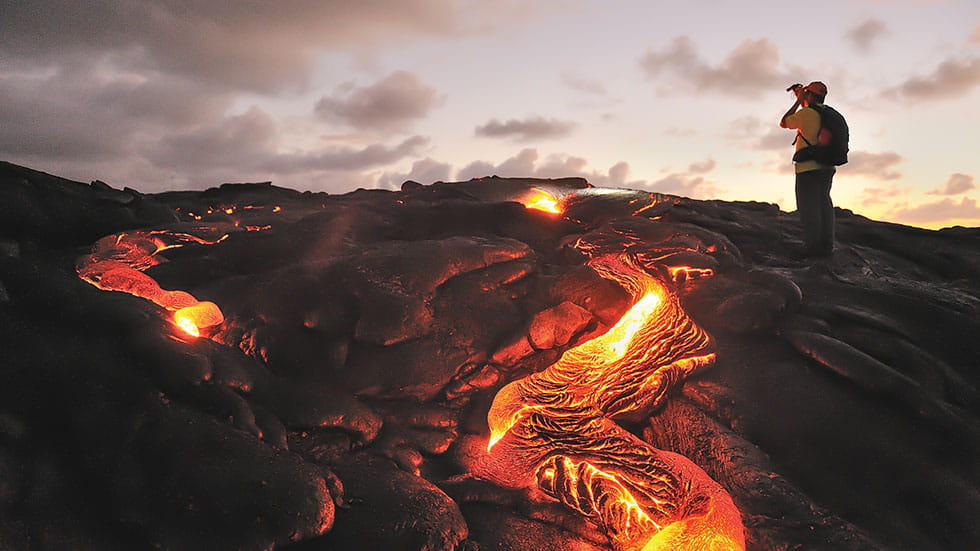 A visitor watches lava flows from Kīlauea Volcano at Hawai‘i Volcanoes National Park. Photo by Tamela/Stock.Adobe.com