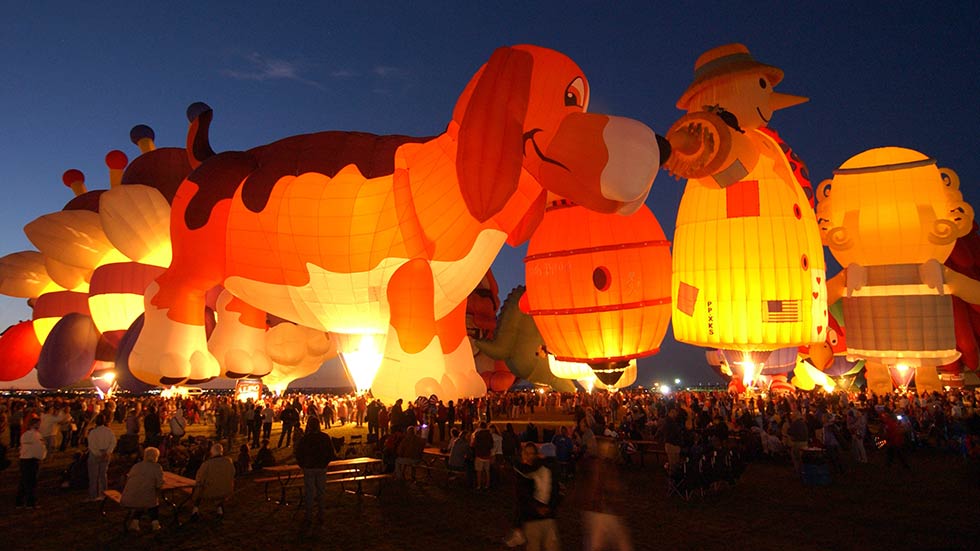 Hot air balloons illuminating The Albuquerque Balloon Festival at night.