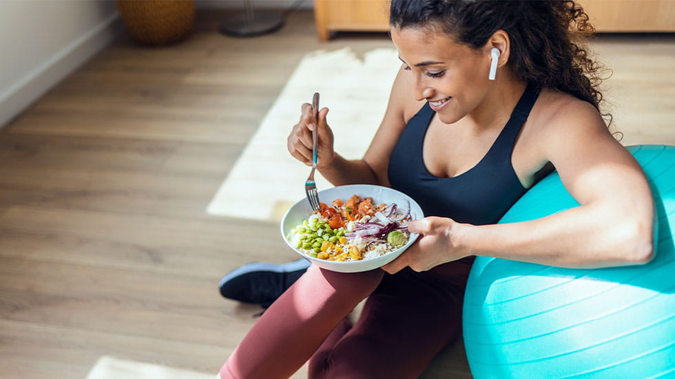 Woman eating salad while leaning on medicine ball