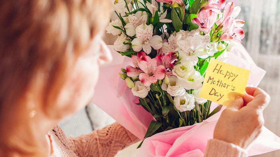 woman holding flowers with note that says happy mothers day