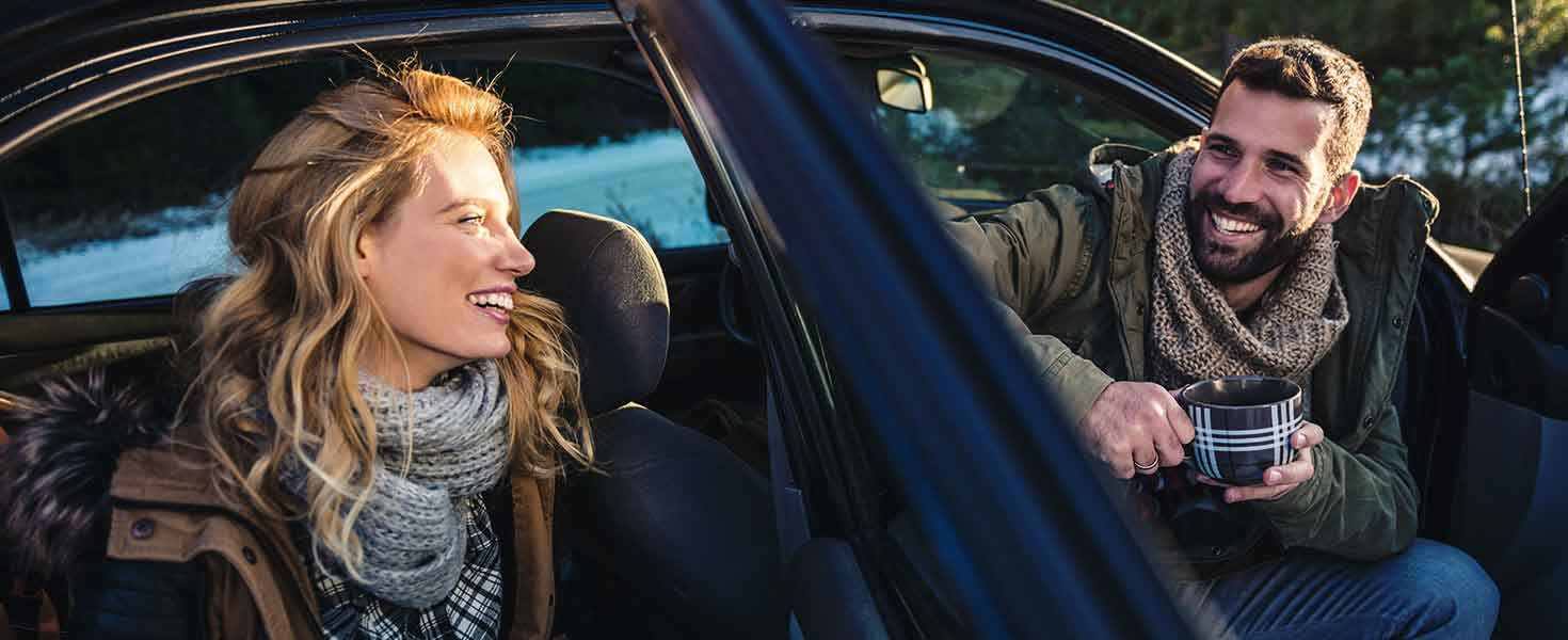 man and woman sitting in car facing out of doors smiling at each other